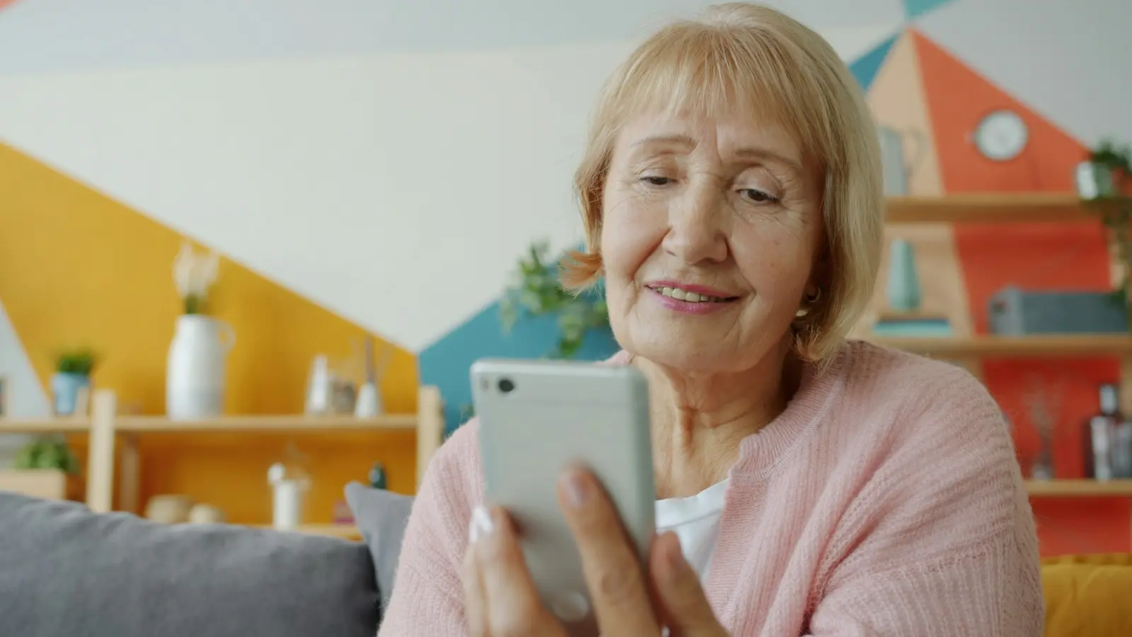 Eine ältere Frau schaut lächelnd auf ihr Smartphone.